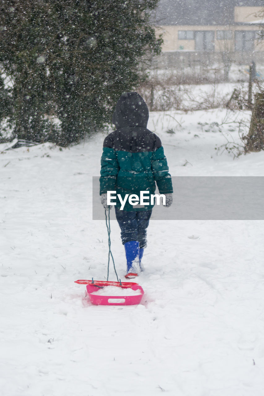 Rear view of girl with sled on snow