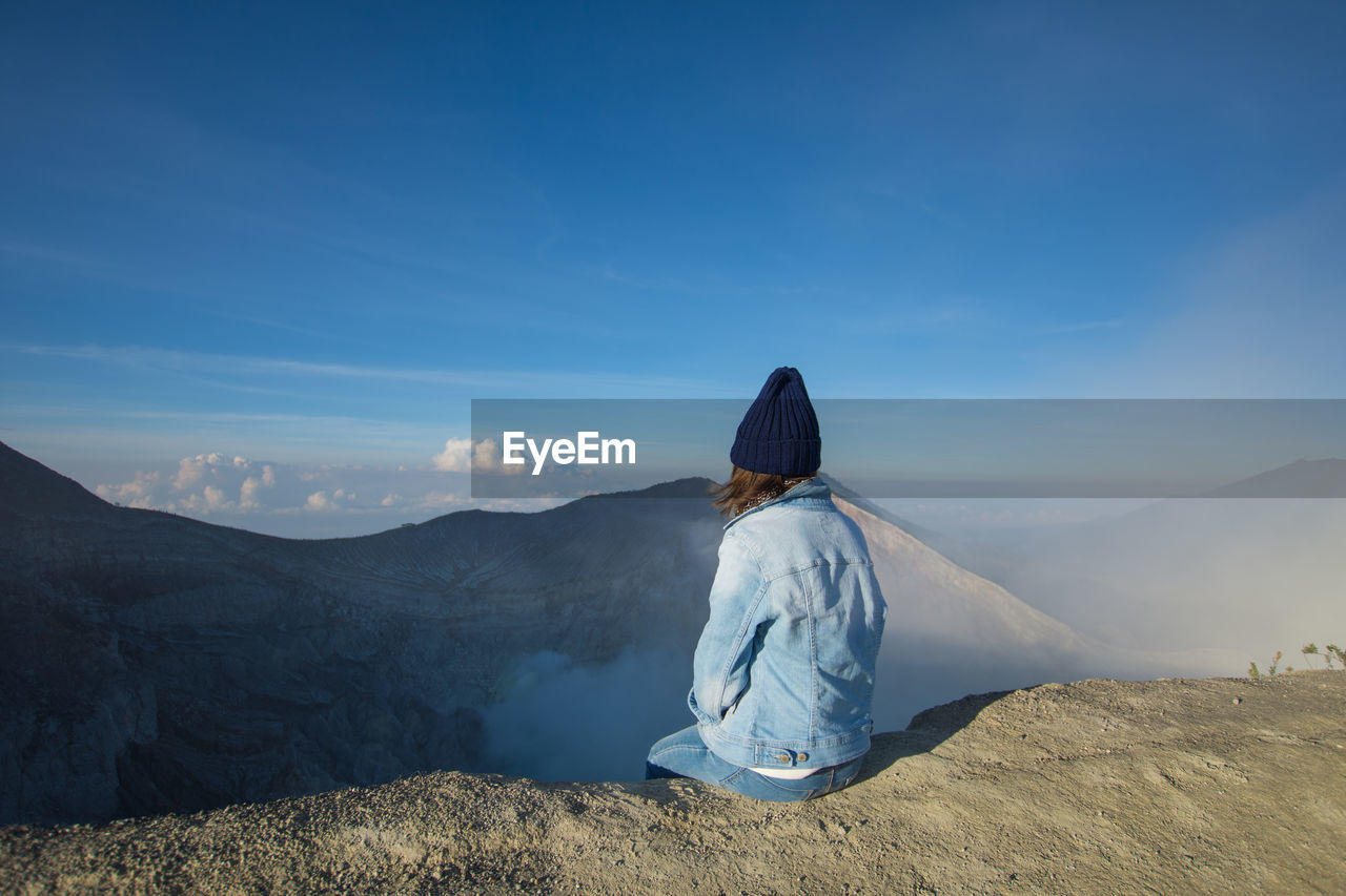 Woman looking at view while sitting on mountain against sky