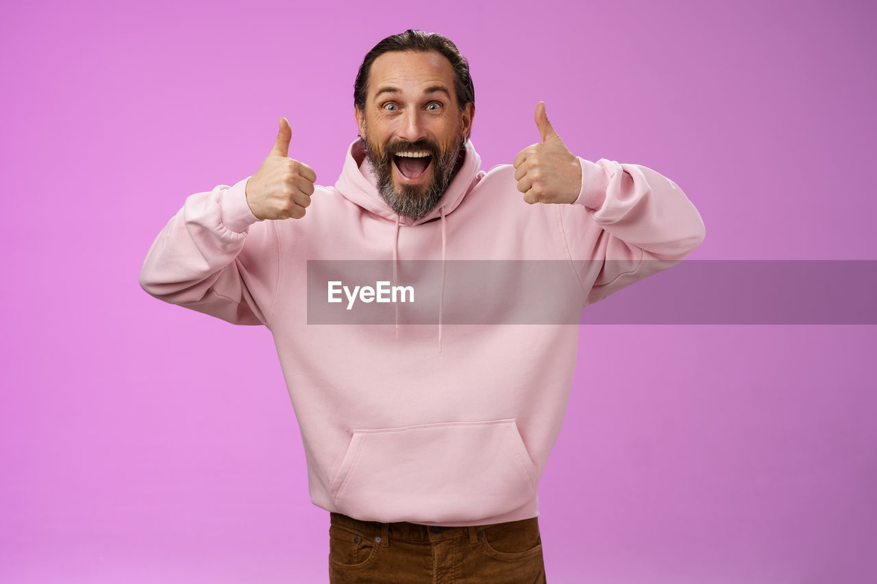 Cheerful man showing thumbs up against purple background