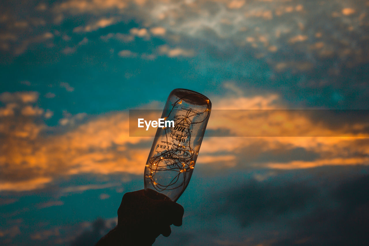 PERSON HOLDING GLASS AGAINST ORANGE SKY