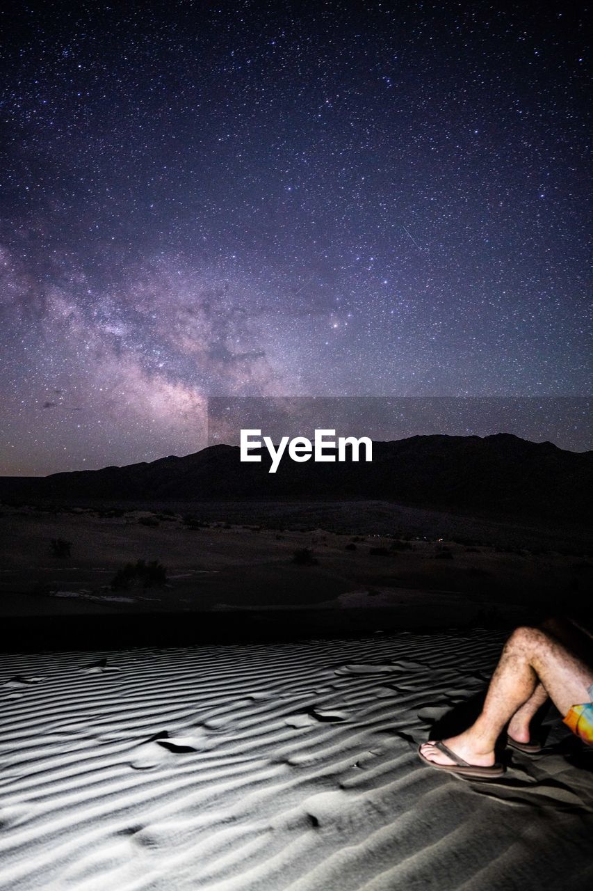 low section of woman sitting on field against sky at night