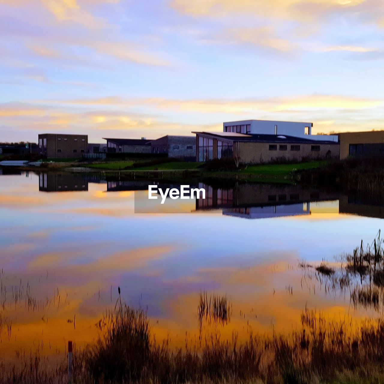 LAKE BY BUILDINGS AGAINST SKY DURING SUNSET