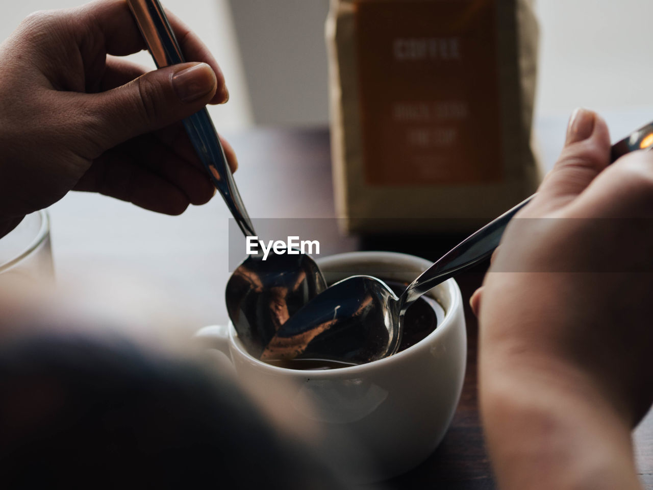 Cropped image of hands holding spoons in black coffee at cafe