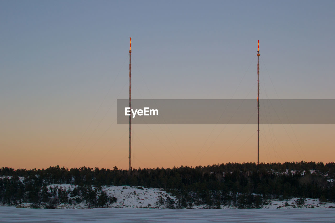 Low angle view of antenna on snowy field against clear sky at dusk