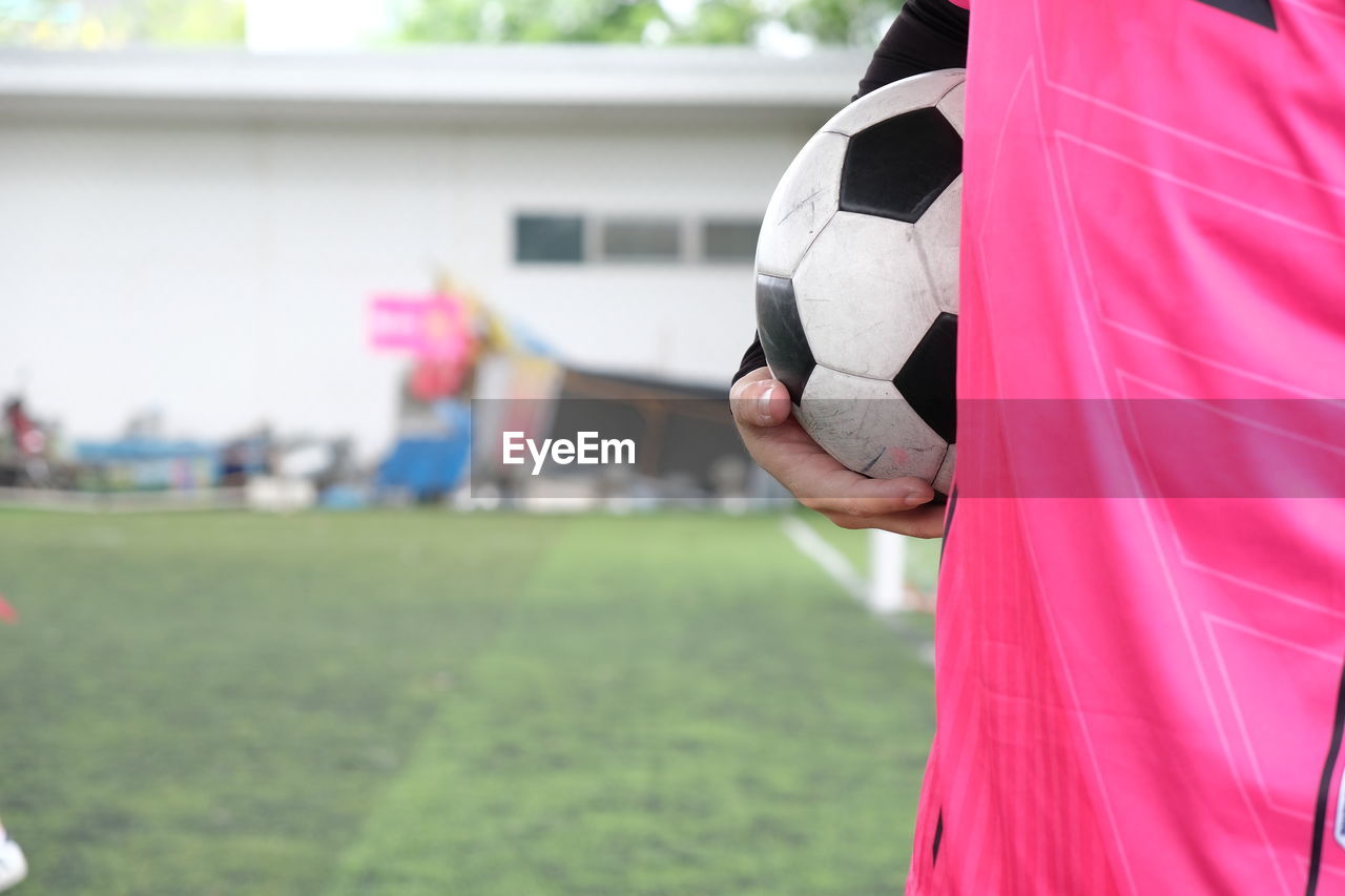 Midsection of man holding playing soccer ball while standing on field