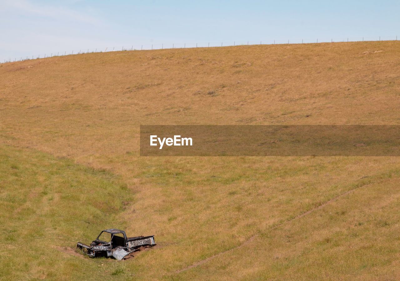 Scenic view of land against sky with an old wrecked truck in a valley 