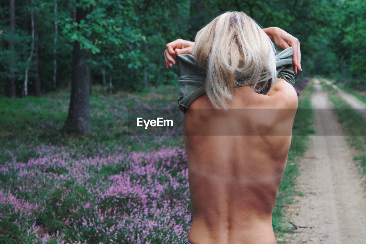 Rear view of woman removing clothes while standing in forest