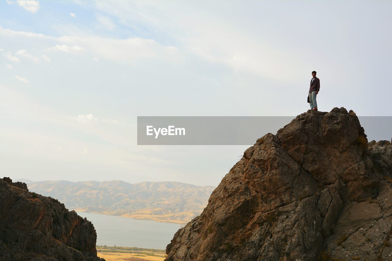 REAR VIEW OF MAN STANDING ON MOUNTAIN