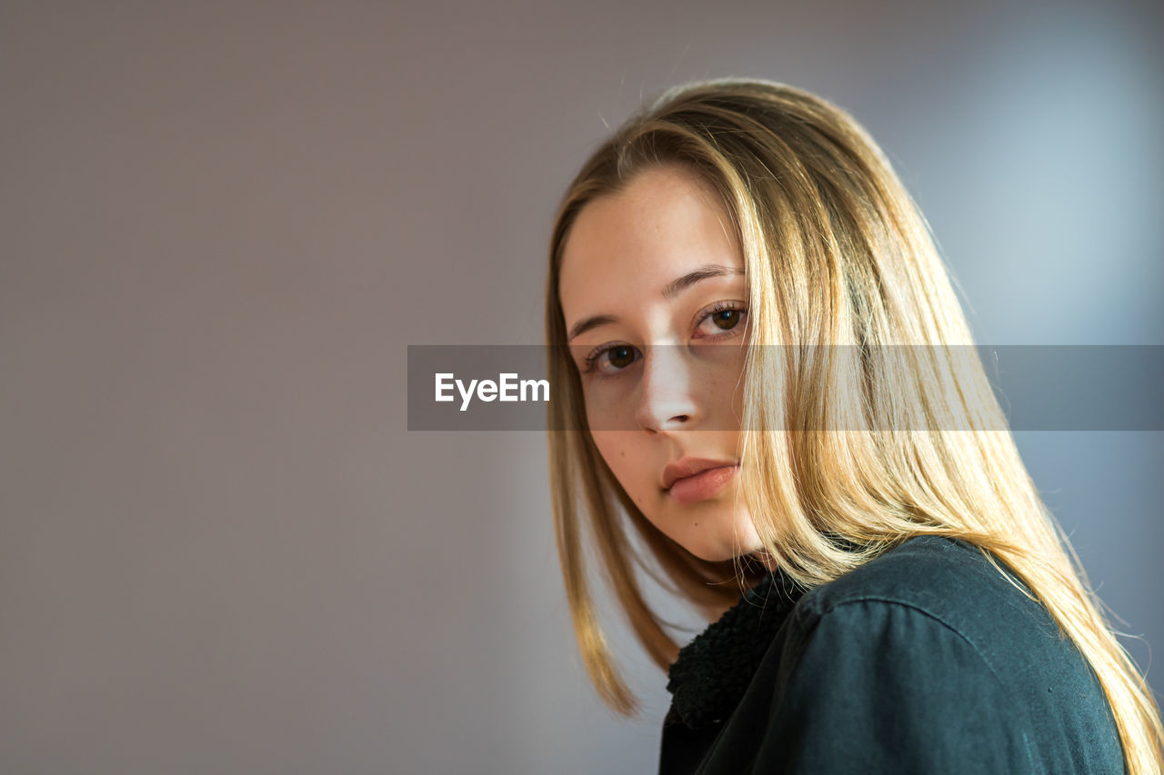 PORTRAIT OF BEAUTIFUL YOUNG WOMAN STANDING AGAINST GRAY BACKGROUND