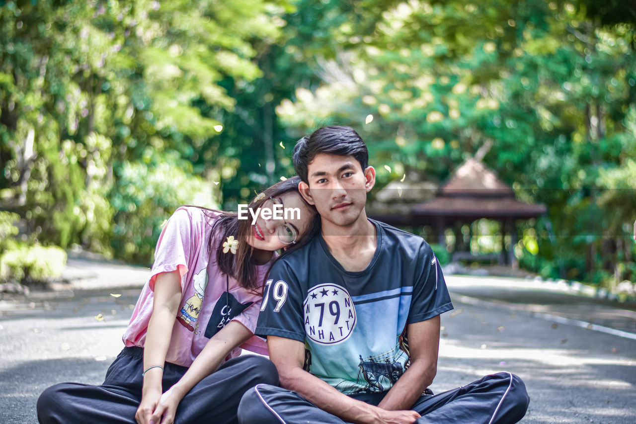 Young couple sitting on footpath while looking at camera