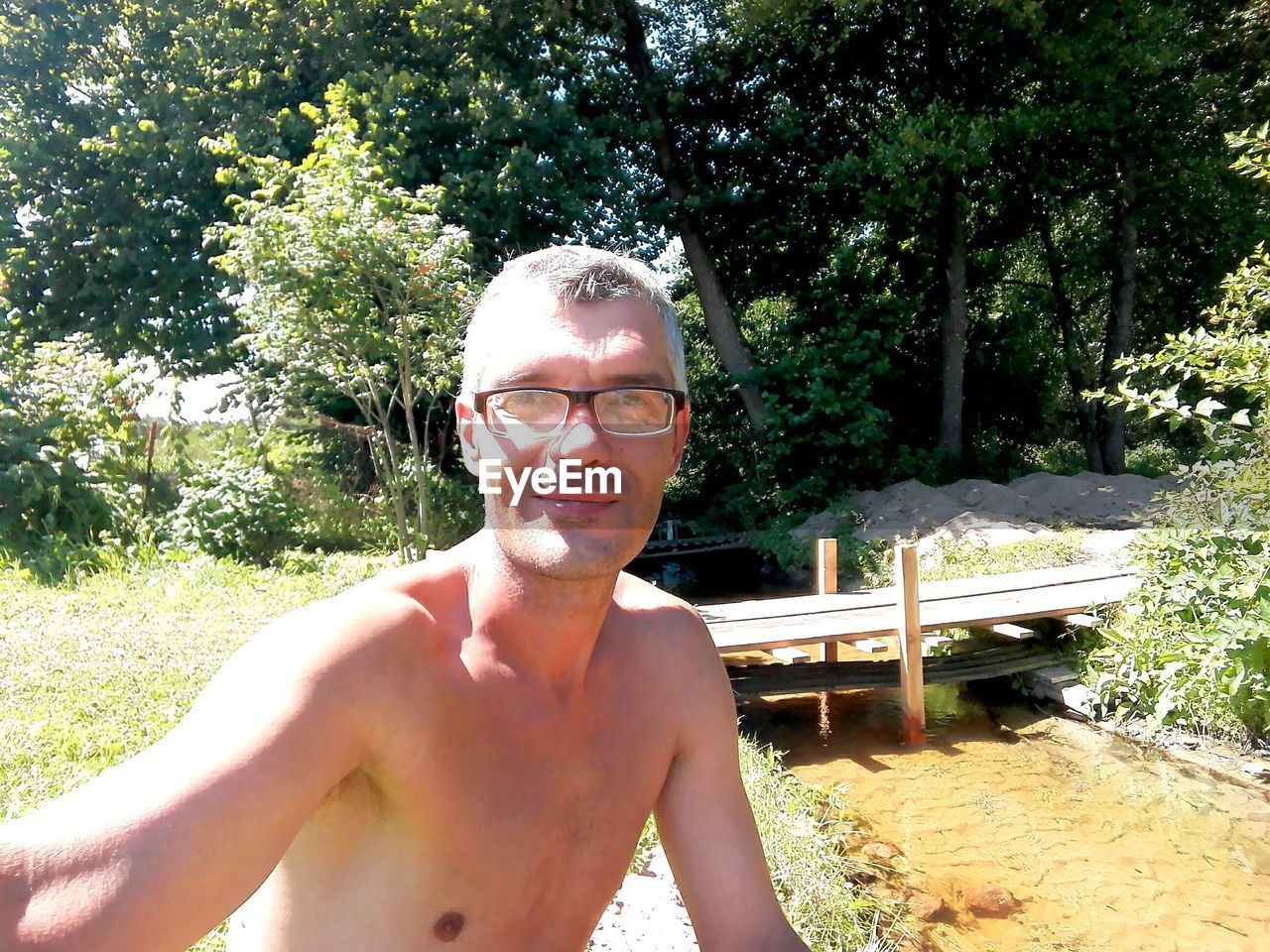 PORTRAIT OF SHIRTLESS MAN WEARING SUNGLASSES AGAINST TREE