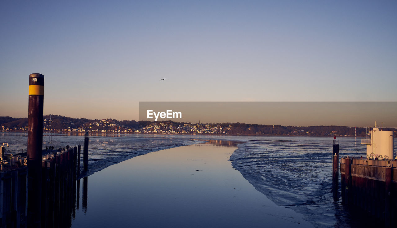 BIRDS FLYING OVER SEA AGAINST BUILDINGS IN CITY