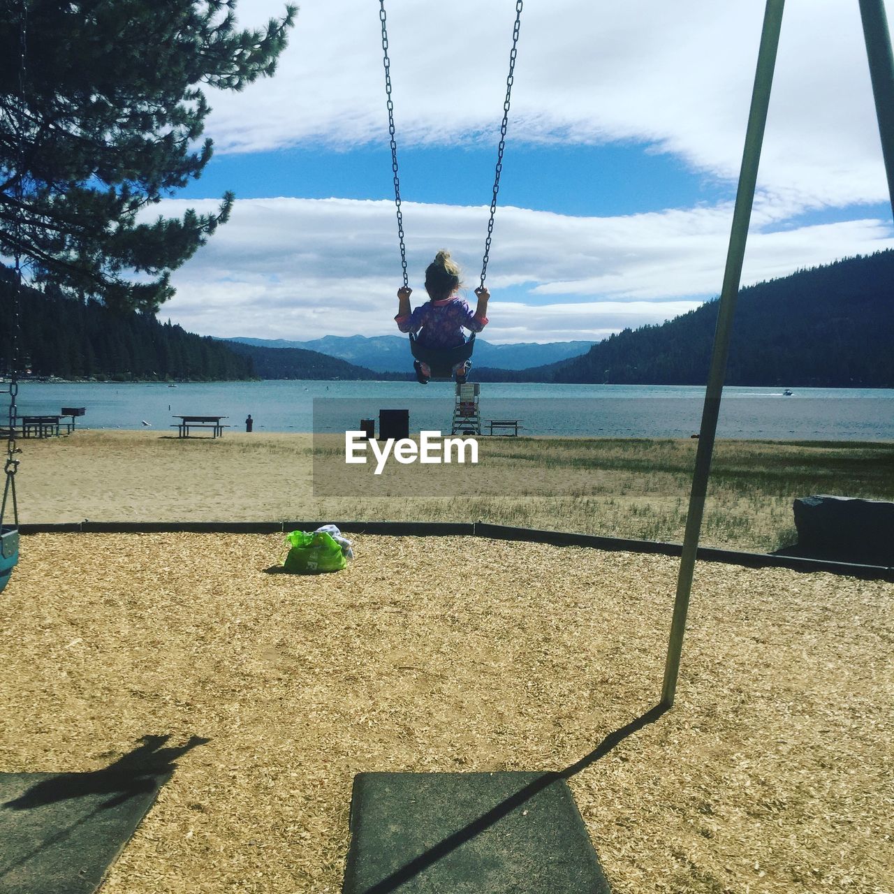 Rear view of  small child on swing on beach with lake against sky