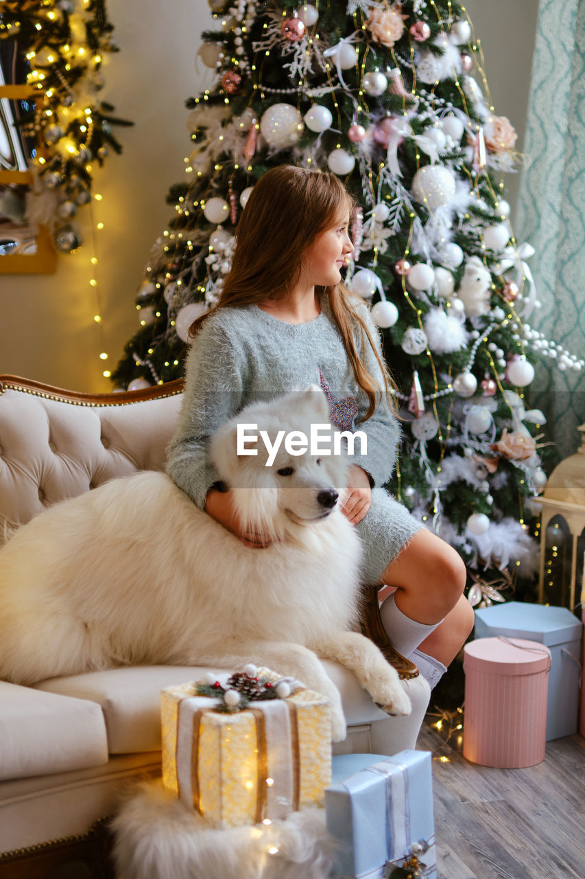 Little cute girl sitting on the sofa with samoyed dog