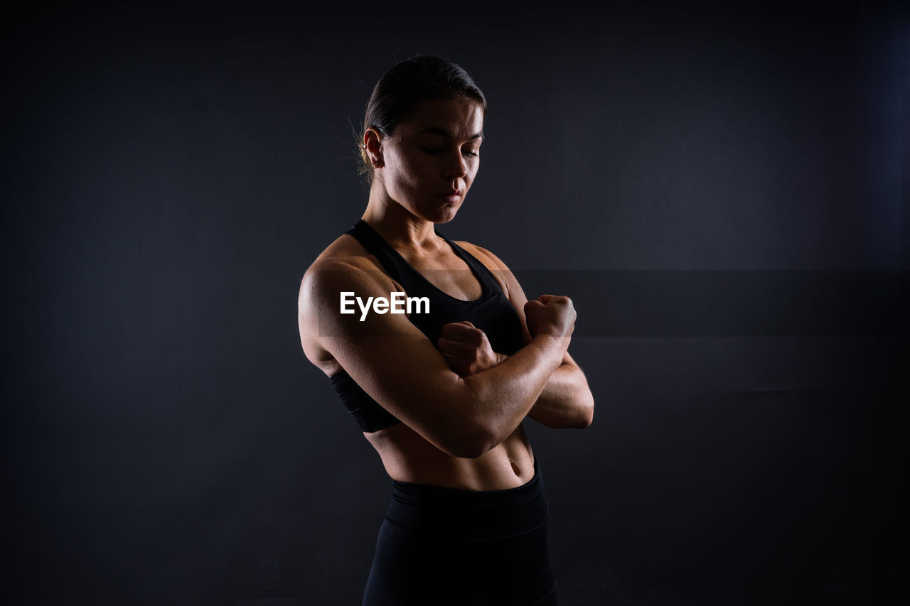 side view of young woman looking away while standing against black background