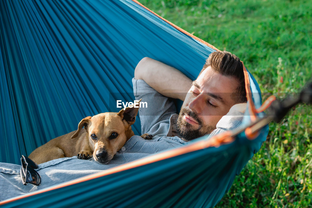 Portrait of attractive european man on hammock with cute sleepy dog.