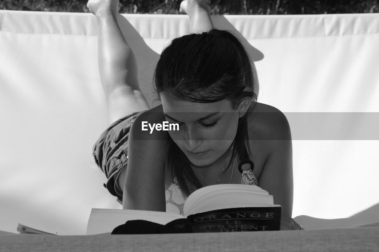 Young woman reading book while lying on hammock