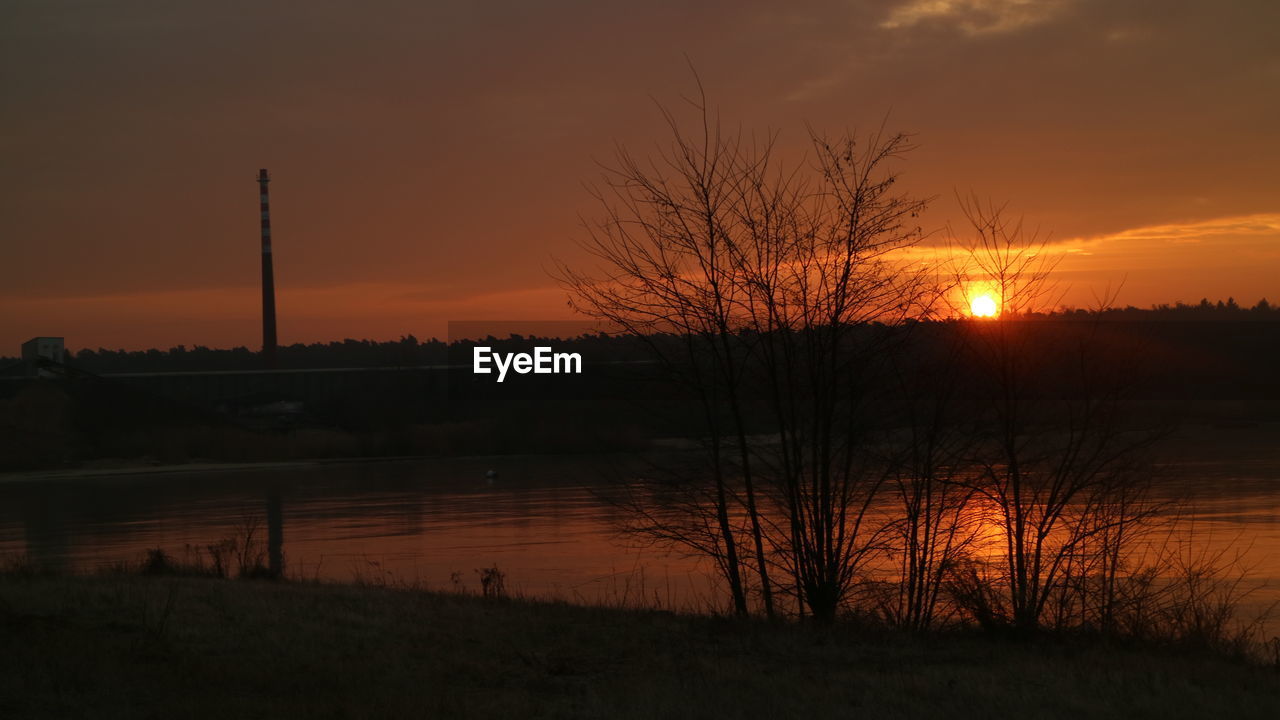 REFLECTION OF SILHOUETTE TREES IN LAKE AGAINST SKY DURING SUNSET