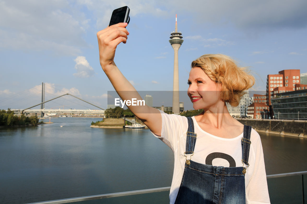 Woman taking selfie with mobile phone against sky