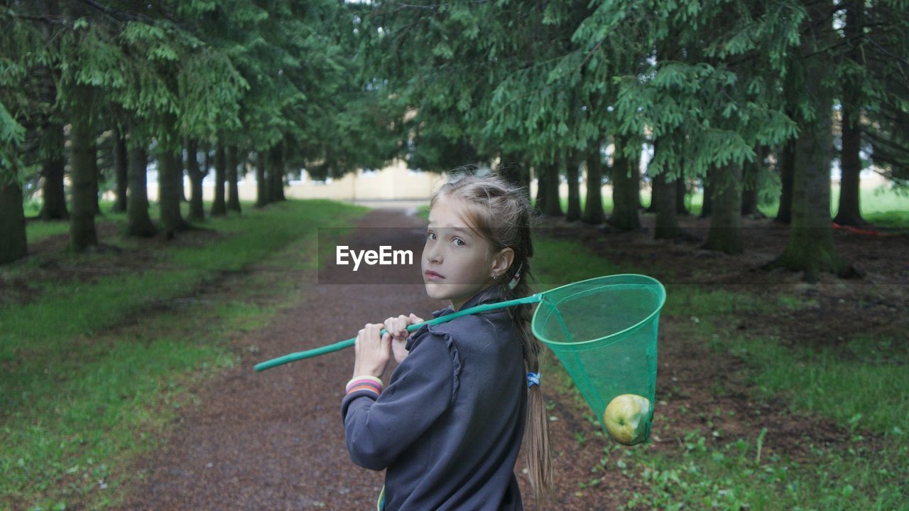 Portrait of girl holding scoop net while standing on field