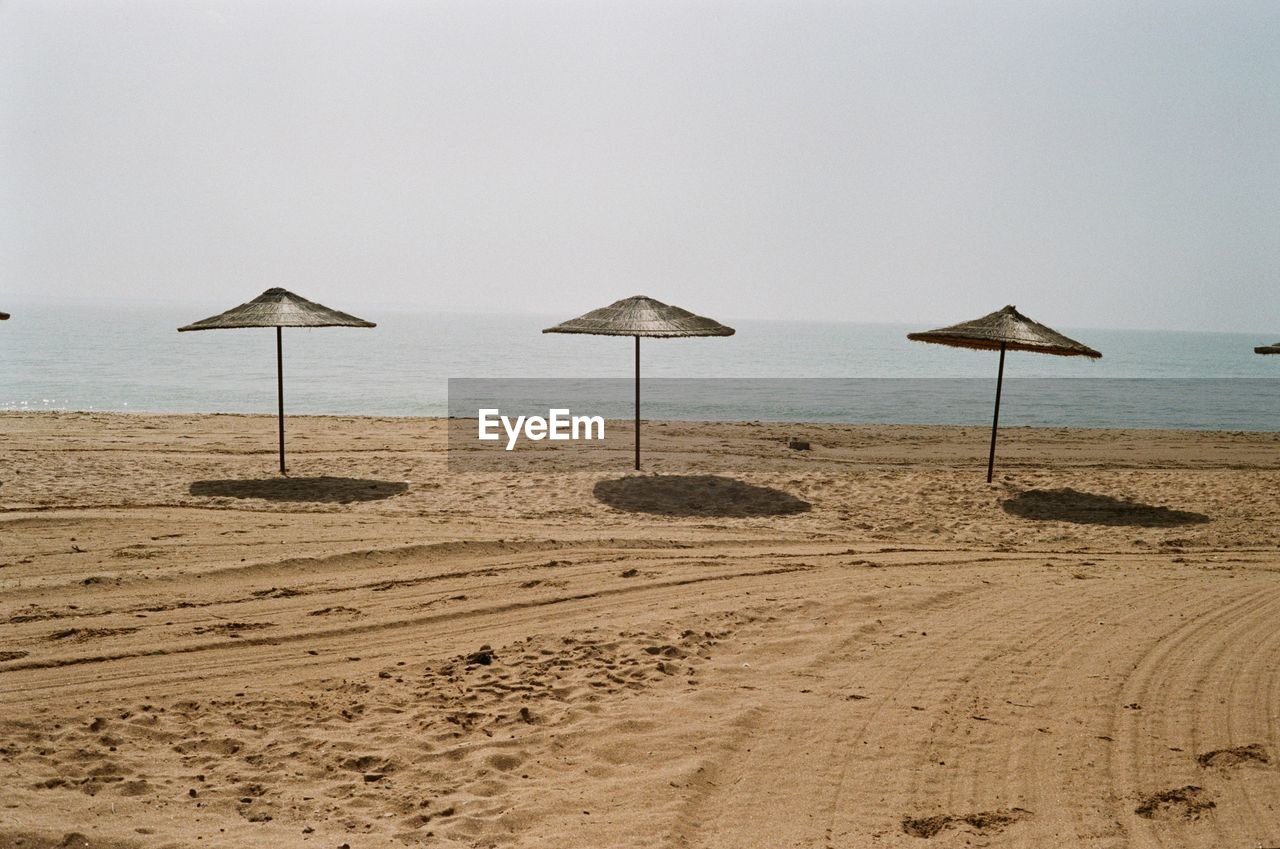 BEACH UMBRELLAS ON SHORE AGAINST SKY