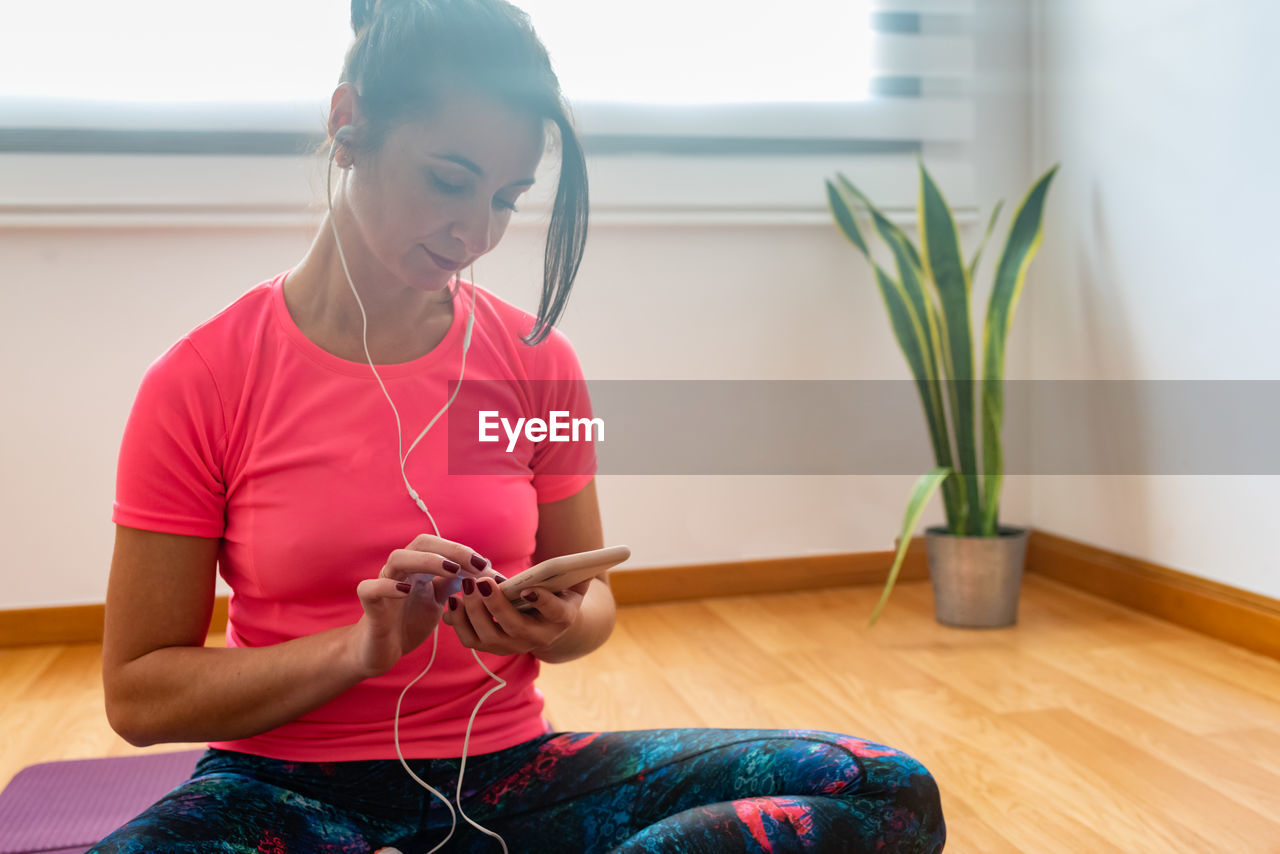 Smiling woman listening music while sitting on floor at home