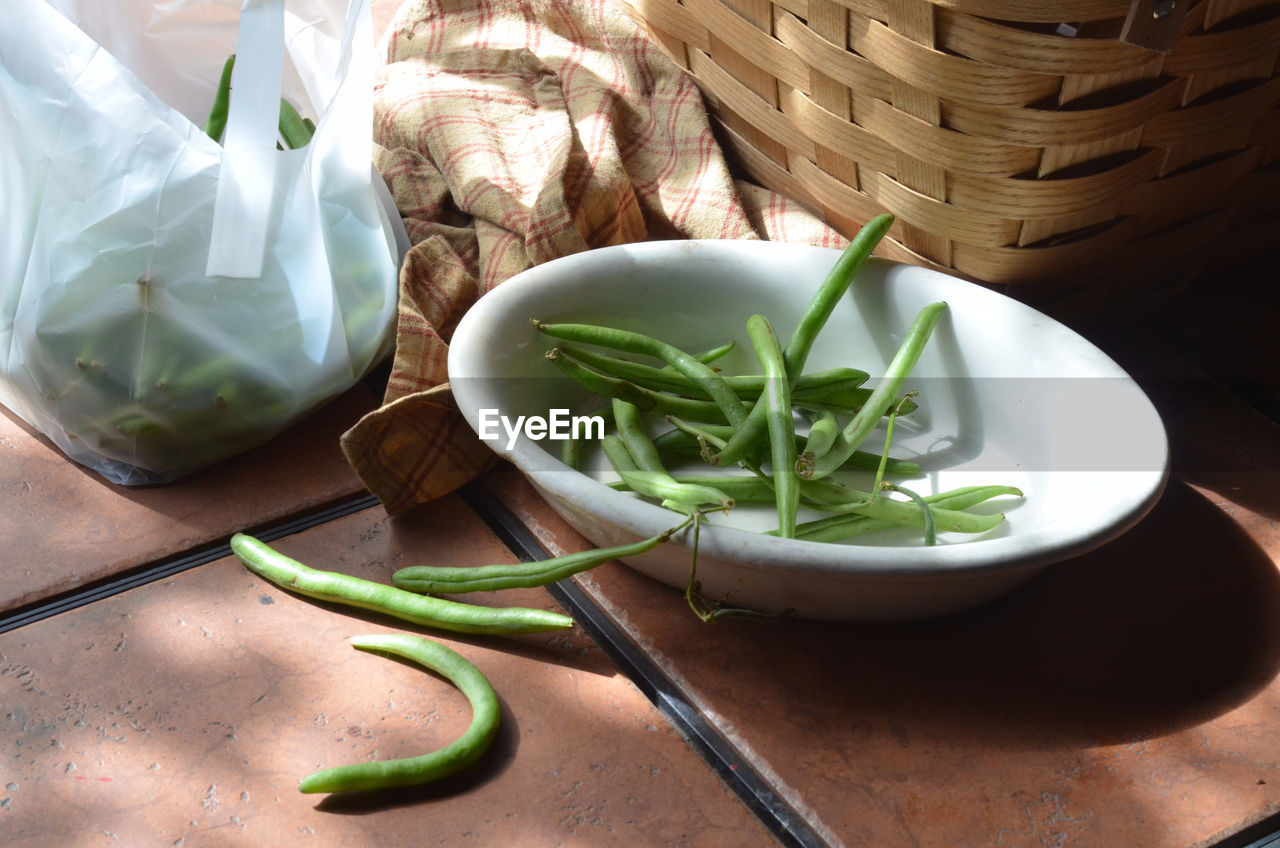 Green beans, white dish with prepared green beans ready for cooking, baske on outdoor table