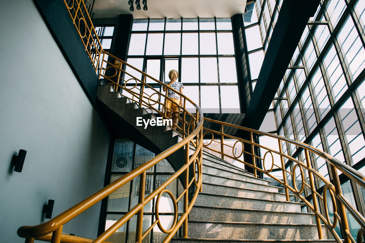 Low angle view of man covering face from hat while standing on staircase