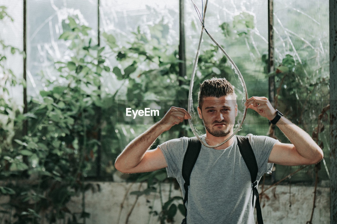 Portrait of young man holding rope standing against plants