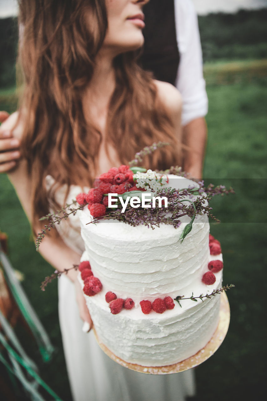 Midsection of couple holding wedding cake at farm