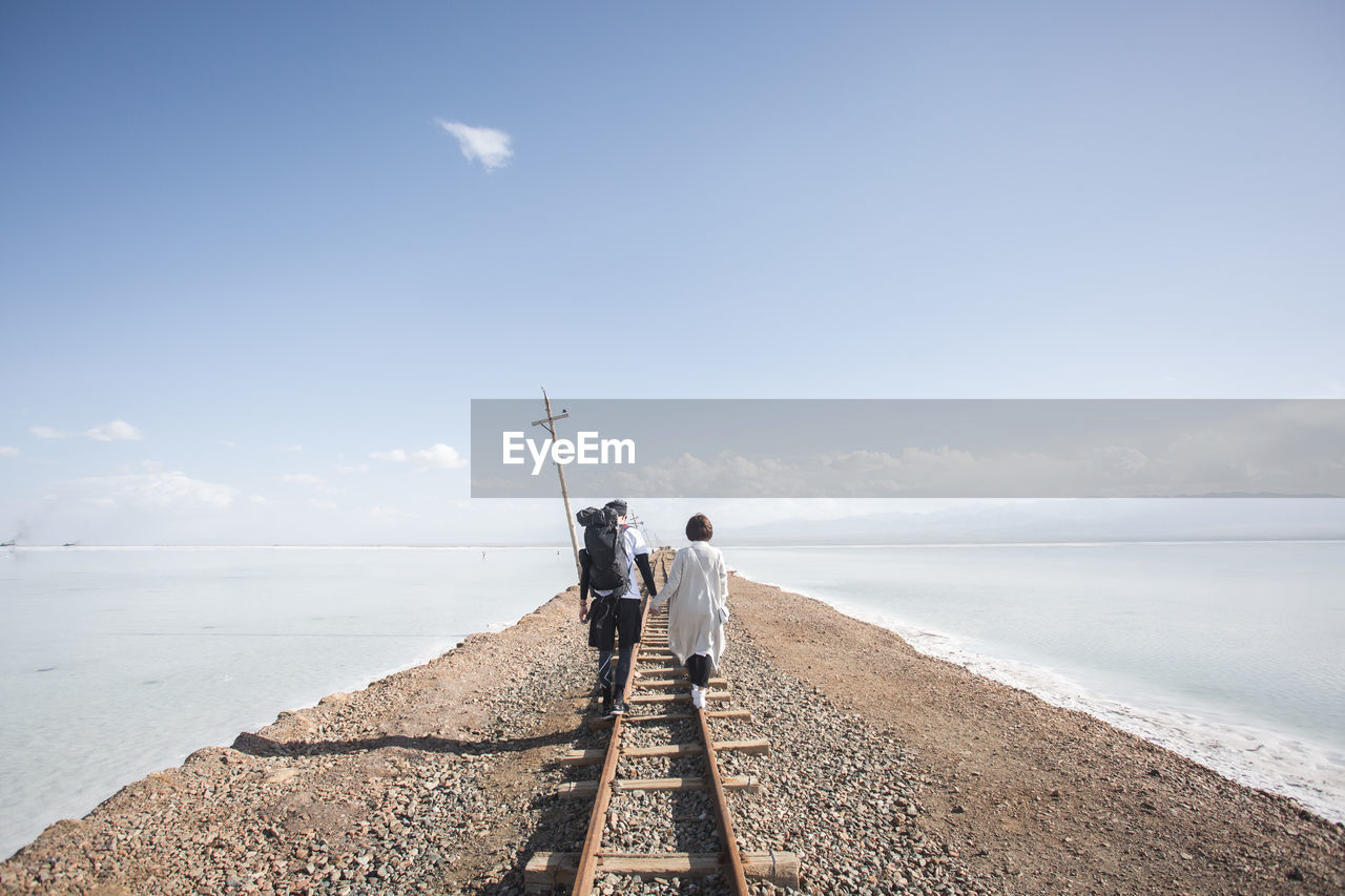 Rear view of couple walking on railroad track against sky