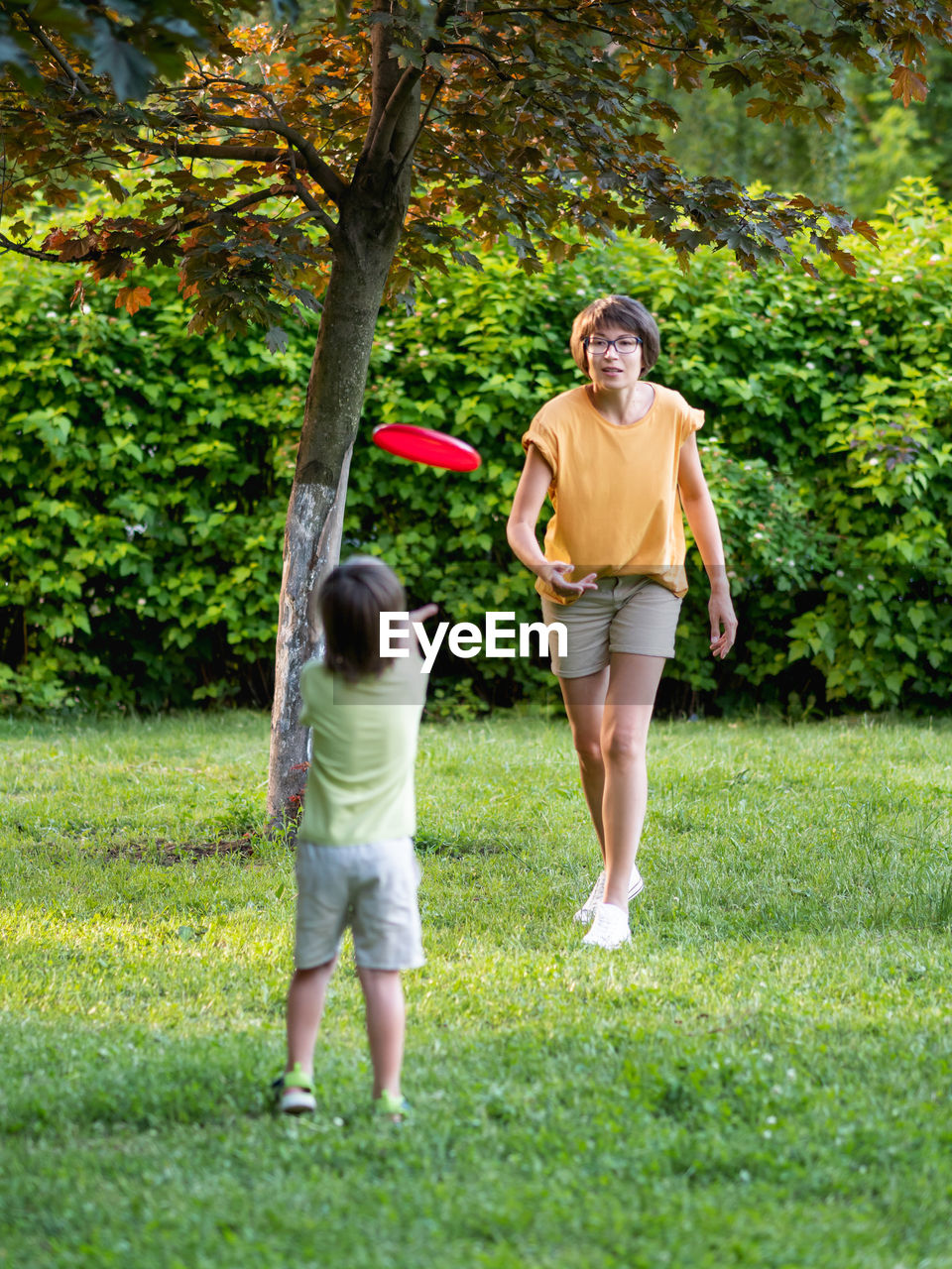 Mother and son play frisbee on grass lawn. outdoor leisure. family life. sports game at backyard.