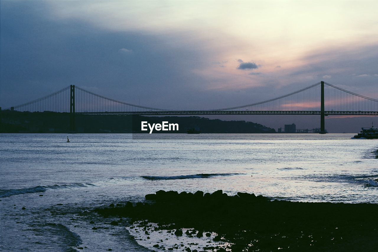 April 25th bridge over tagus river against cloudy sky during sunset