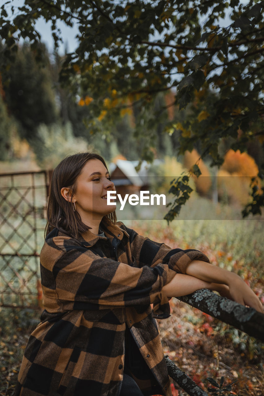 Young woman looking away while standing on tree during autumn