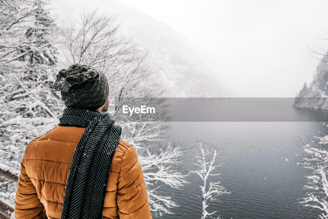 Rear view of man standing on viewpoint over lake in winter, snow, nature, hiking.