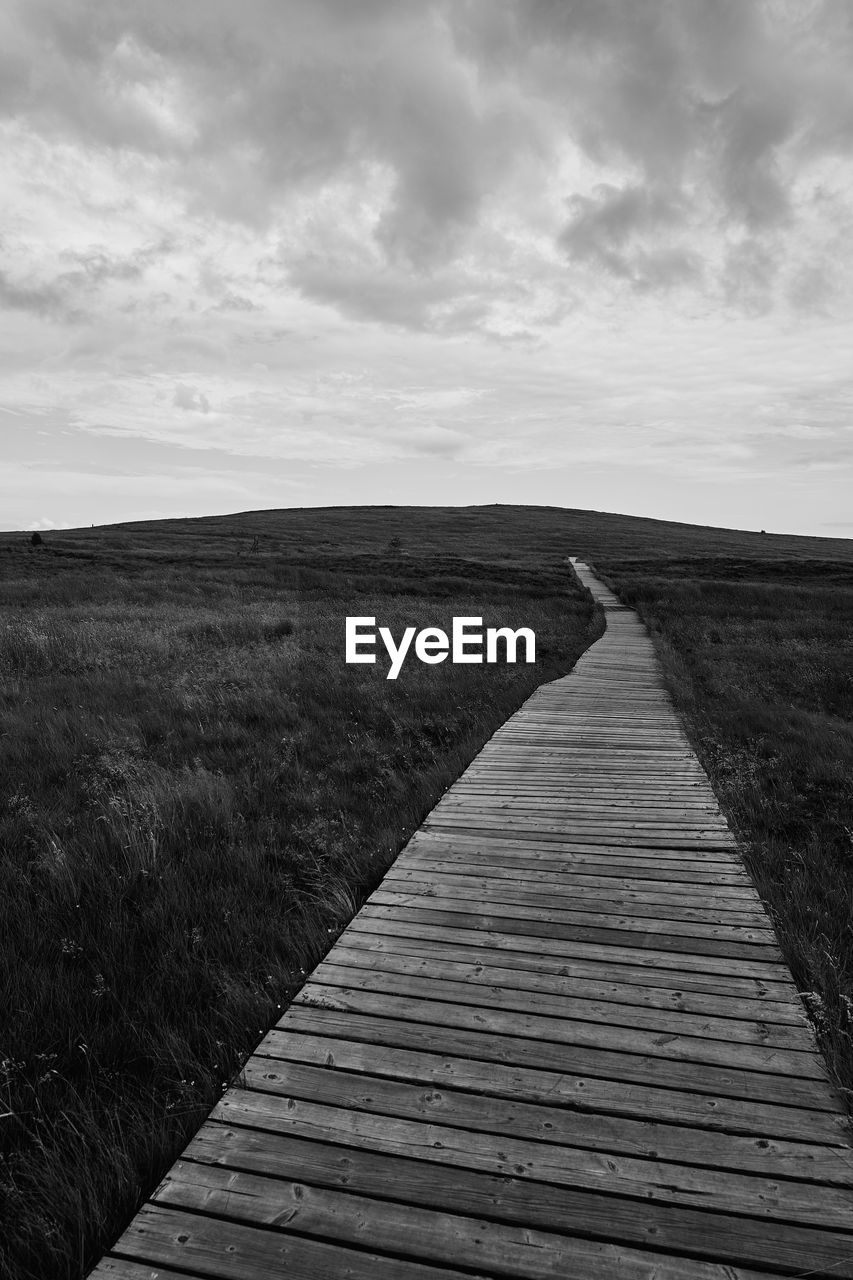 Boardwalk leading towards landscape against sky