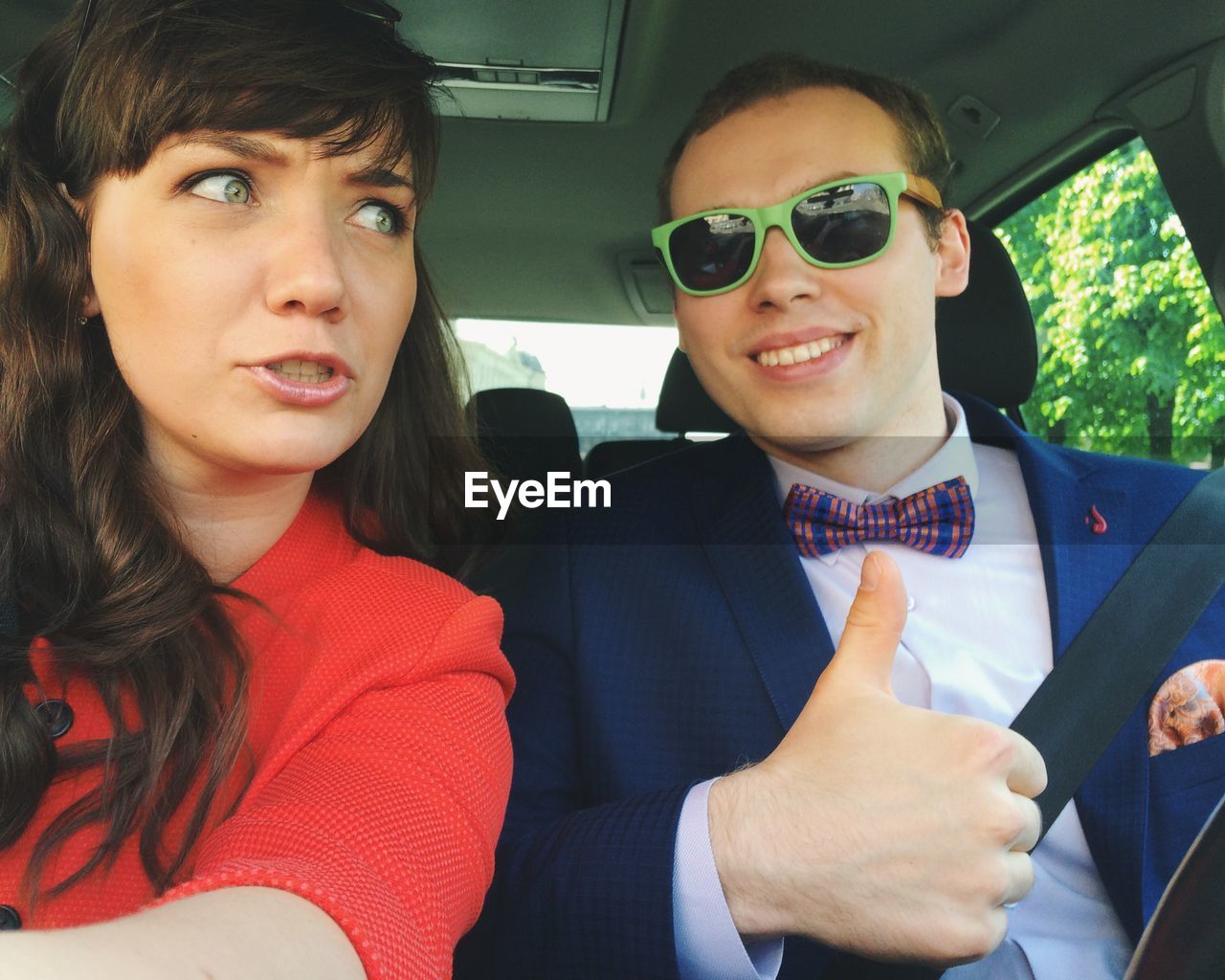 Smiling young man with woman showing thumbs up sign in car