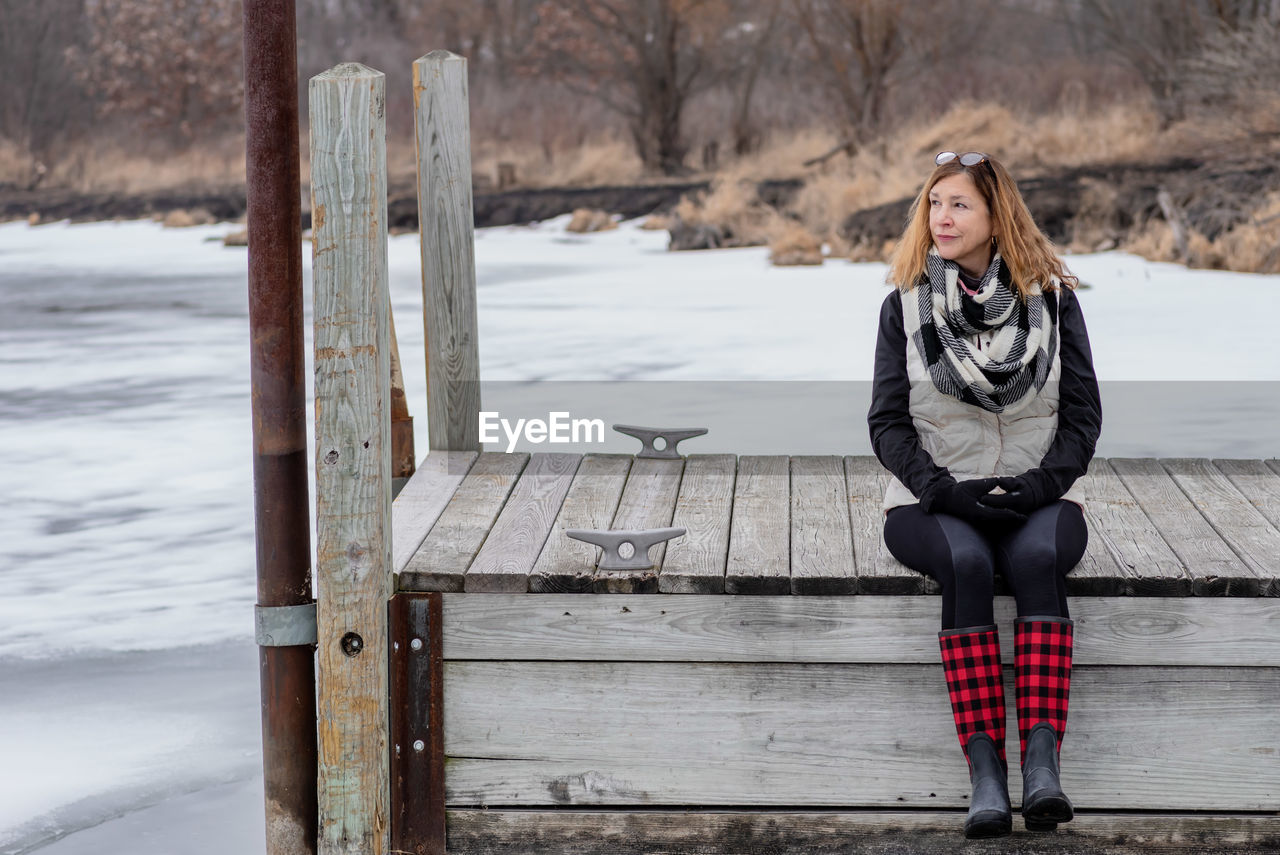 Thoughtful woman sitting on pier over frozen lake