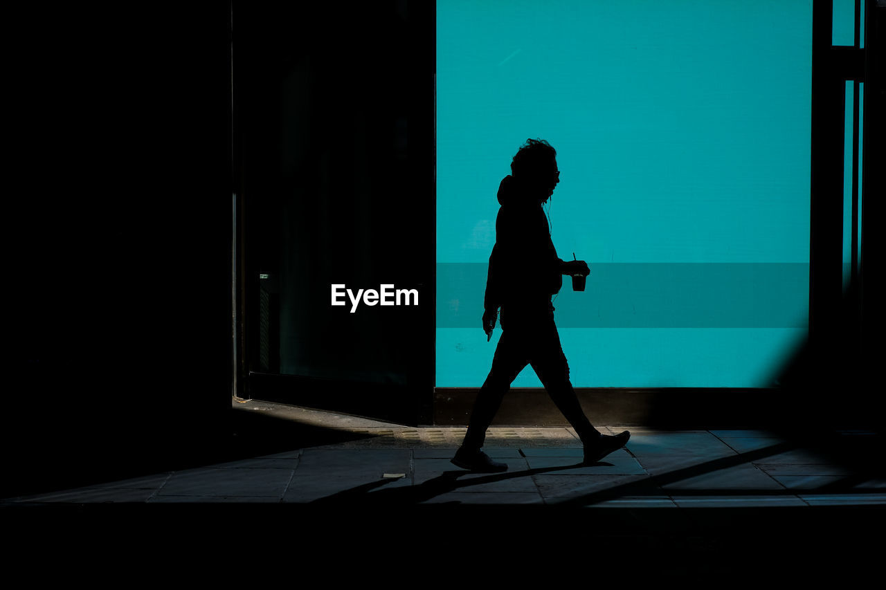 Side view silhouette of a man walking with a drink