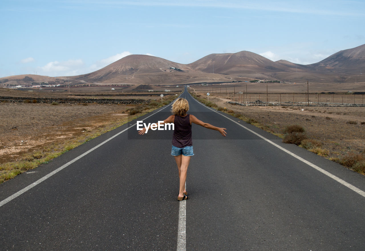 Rear view of woman with arms outstretched walking on country road