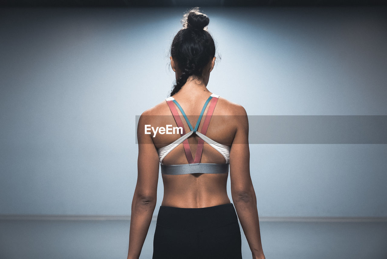 Rear view of female athlete standing against wall in gym