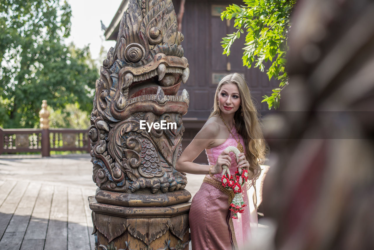 Portrait of smiling young woman outside temple against building