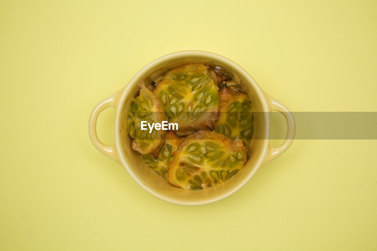 Directly above view of lemon cucumber in bowl on yellow background