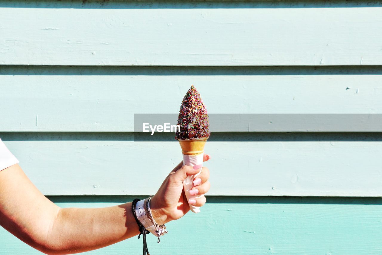 Cropped hand holding ice cream come against wall