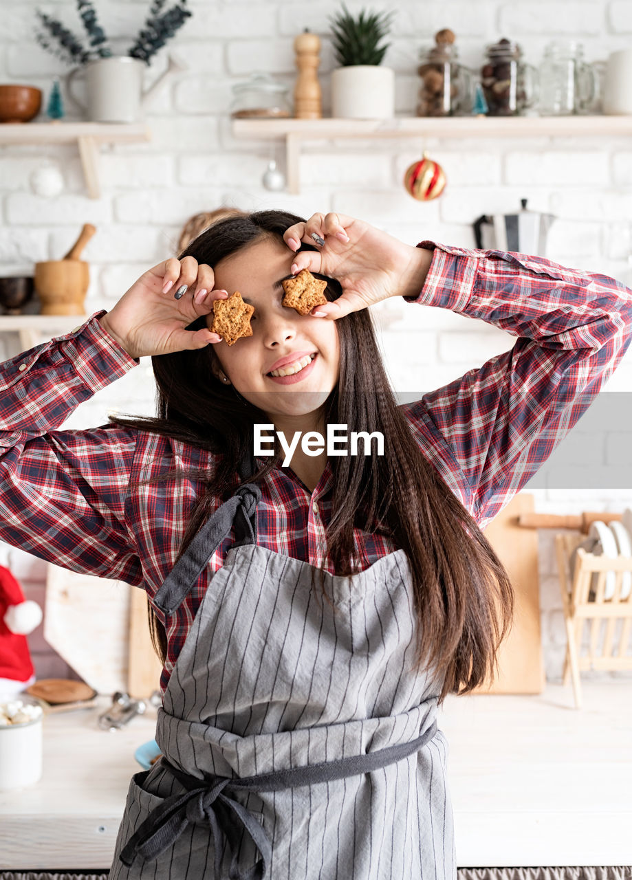 Smiling young woman holding cookie while standing in kitchen