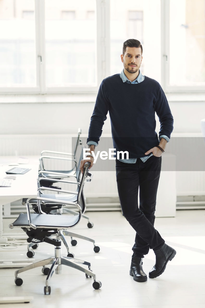 Full length portrait of confident businessman leaning on office chair