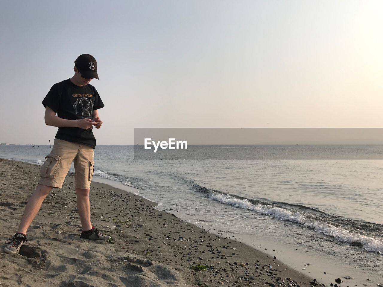 Full length of teenager boy standing at beach against clear sky