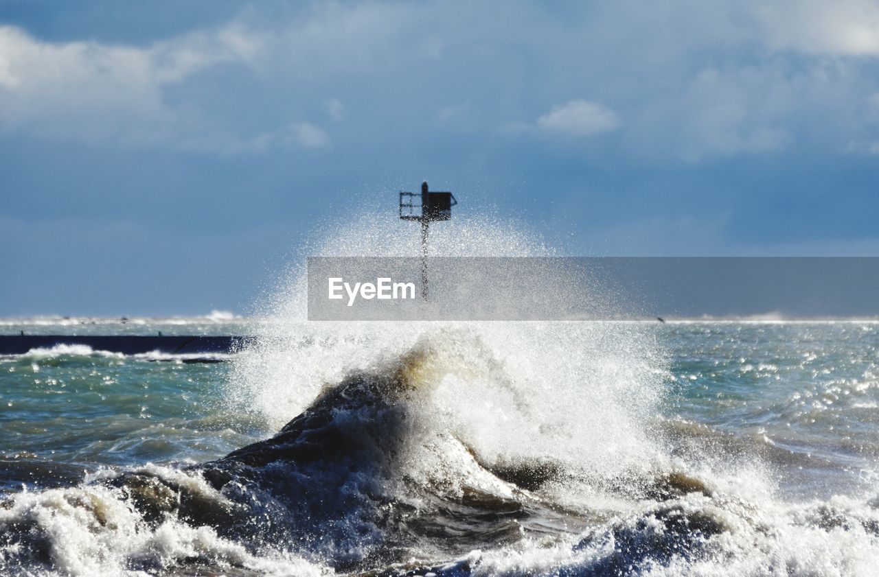 VIEW OF WAVES SPLASHING ON SEA AGAINST SKY