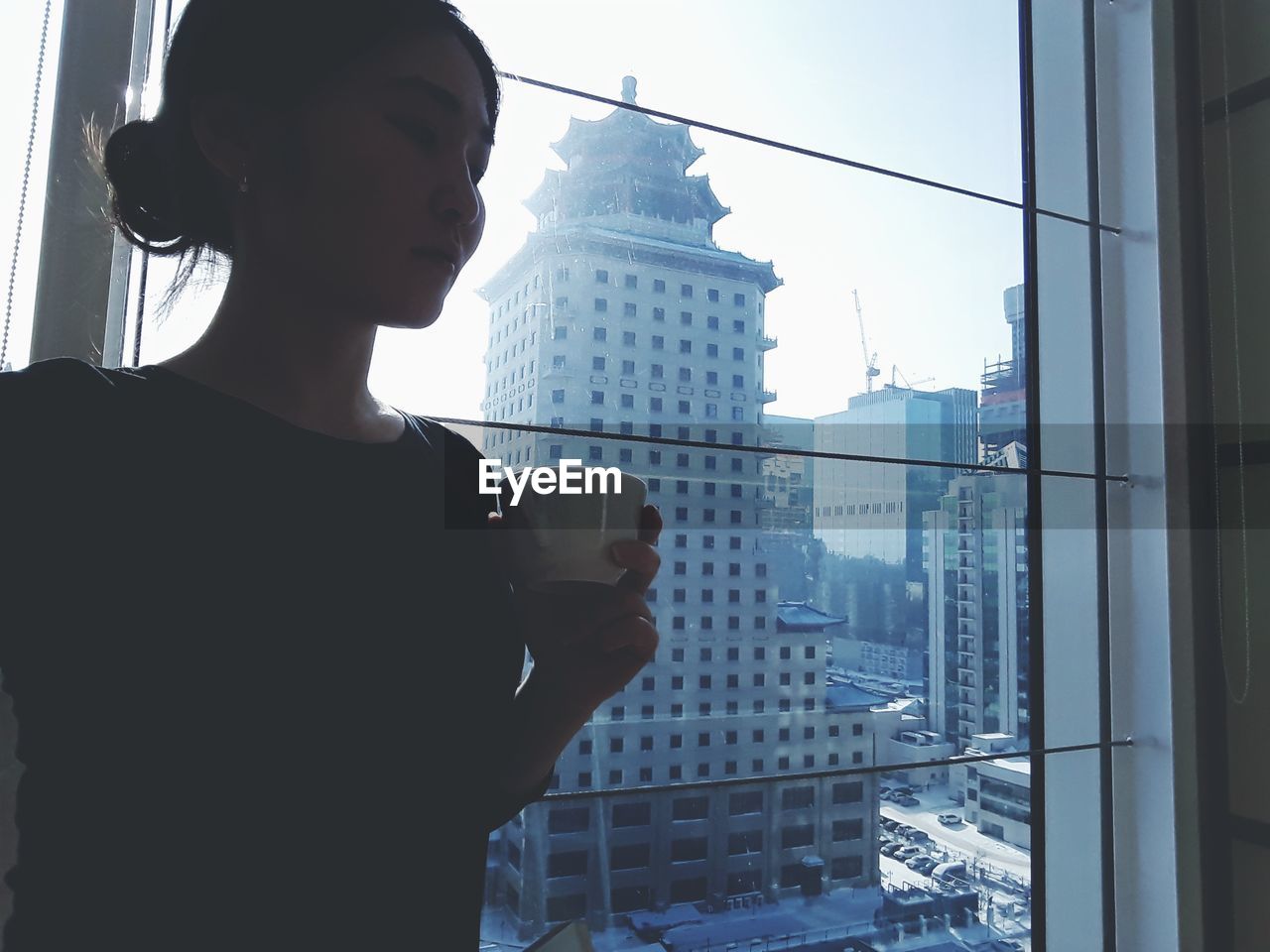 Woman holding coffee cup while standing against window