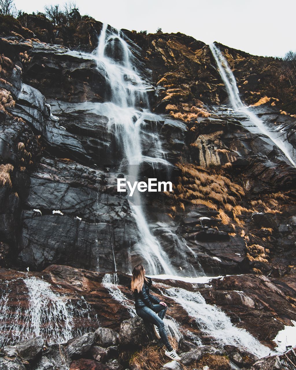 Full length of woman sitting on mountain by waterfall